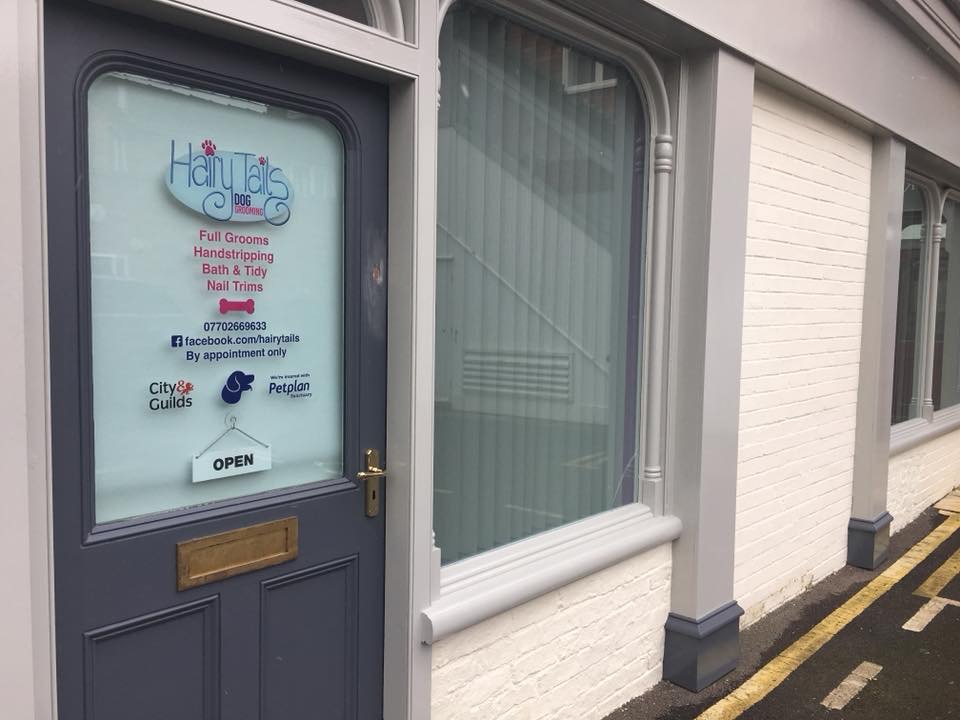 The grey front door of Hairy Tails Dog Grooming with the logo and services on the glass